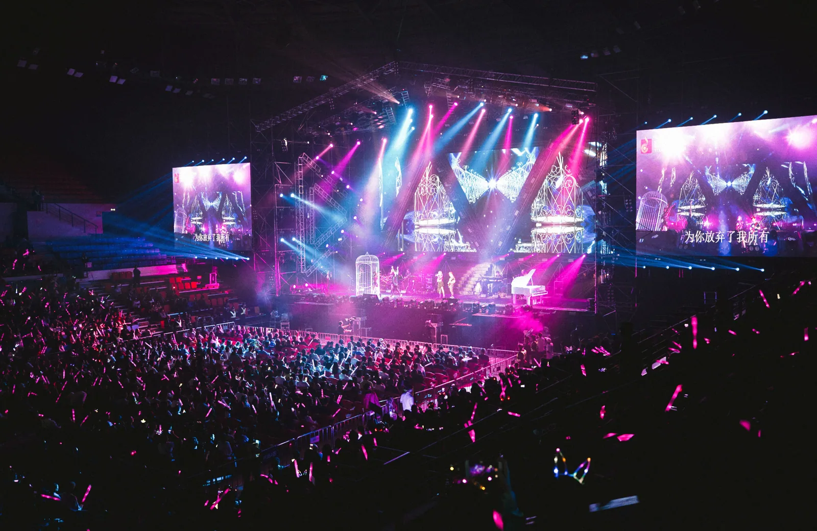 Un concierto reúne al público frente a un escenario iluminado en rosa y azul.